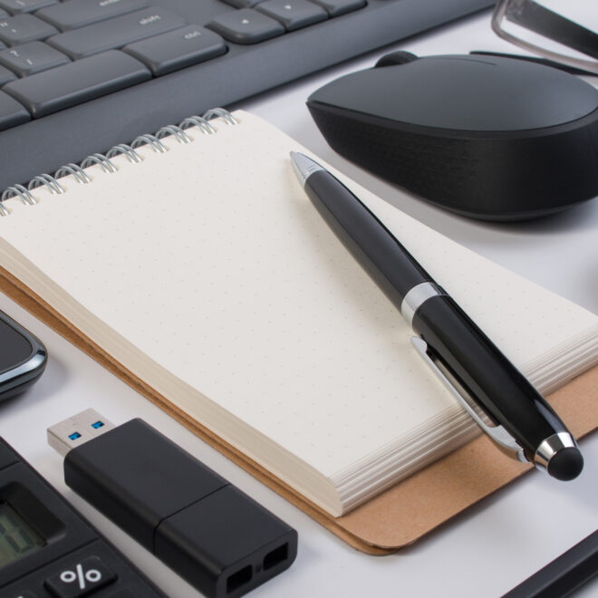 A table of office supplies - notepad, pen, memory stick, keyboard, mouse