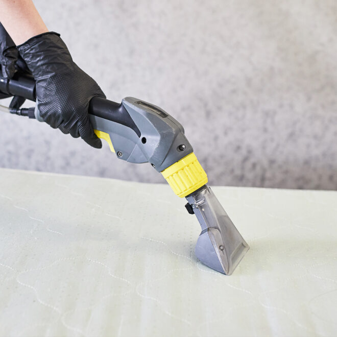 A woman cleaning a mattress with an upholstery attachments