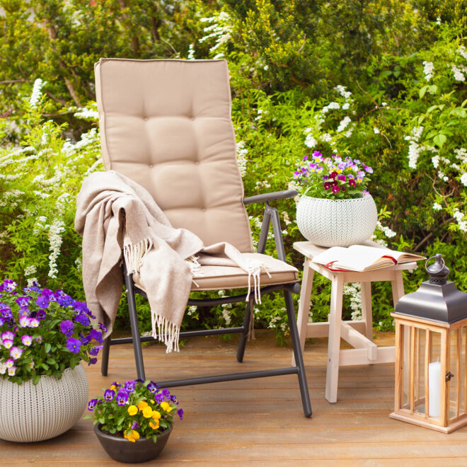 A white garden chair surrounded by potted plants and garden lamps