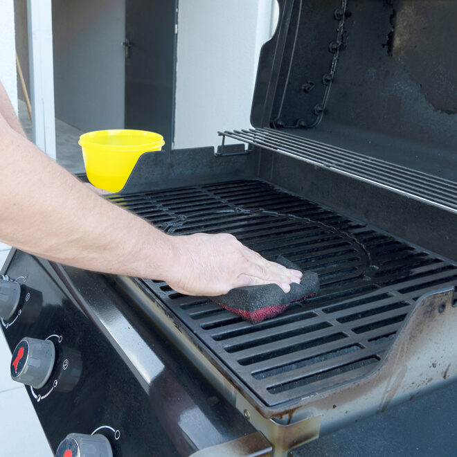 A man using a wire sponge to clean his BBQ grill