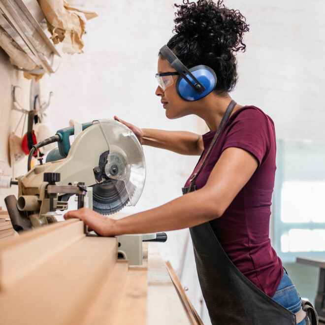 Woman cutting wood with mitre saw in studio