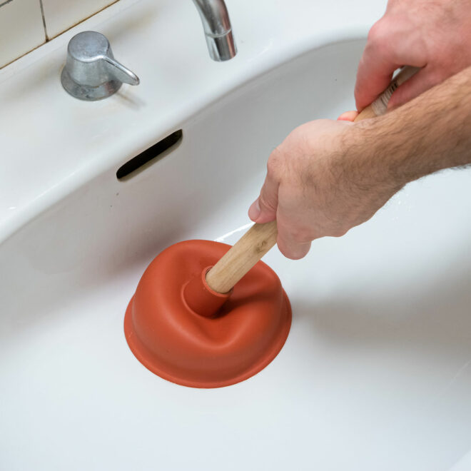 male hand holding a plunger unclogging a bathroom sink