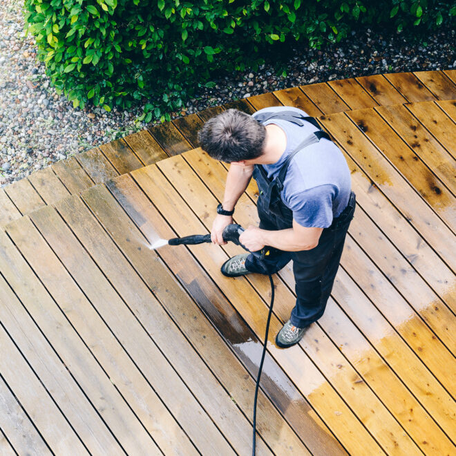 man cleaning terrace with a power washer - high water pressure cleaner on wooden terrace surface